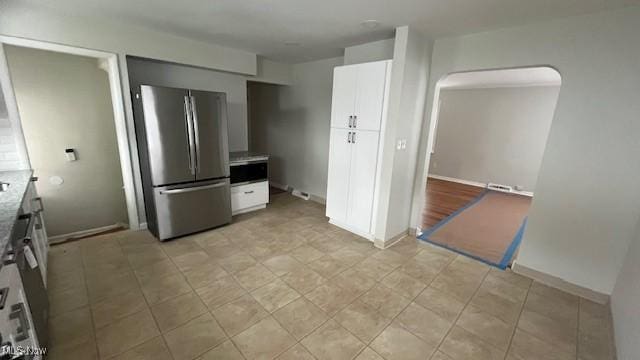 kitchen featuring arched walkways, light countertops, freestanding refrigerator, and white cabinets