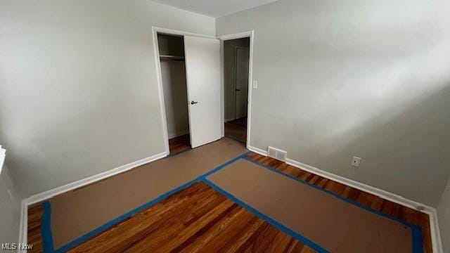 unfurnished bedroom with a closet, wood finished floors, visible vents, and baseboards