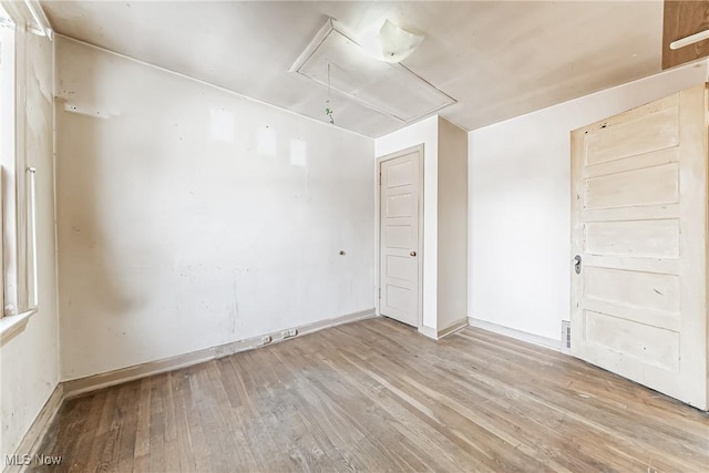 spare room featuring wood finished floors, attic access, and baseboards