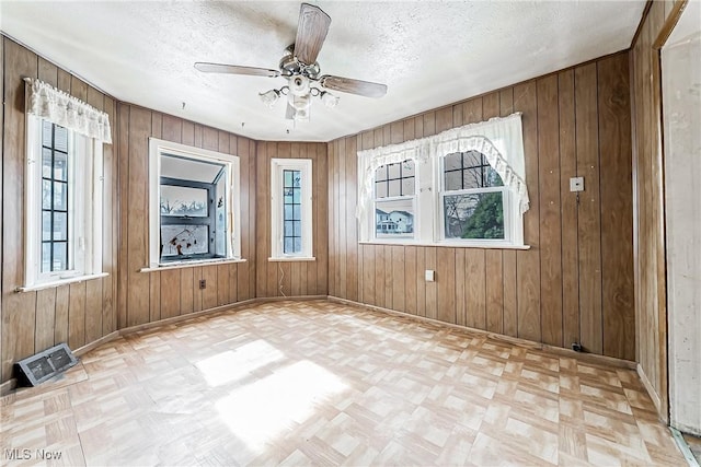 spare room featuring wooden walls, baseboards, visible vents, ceiling fan, and a textured ceiling