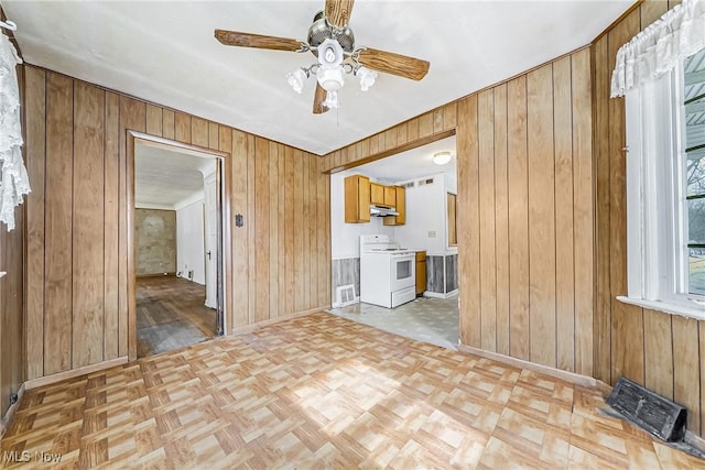 unfurnished room with ceiling fan, wood walls, visible vents, and baseboards