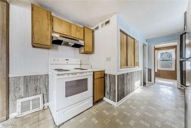 kitchen featuring white electric stove, under cabinet range hood, a wainscoted wall, visible vents, and brown cabinets