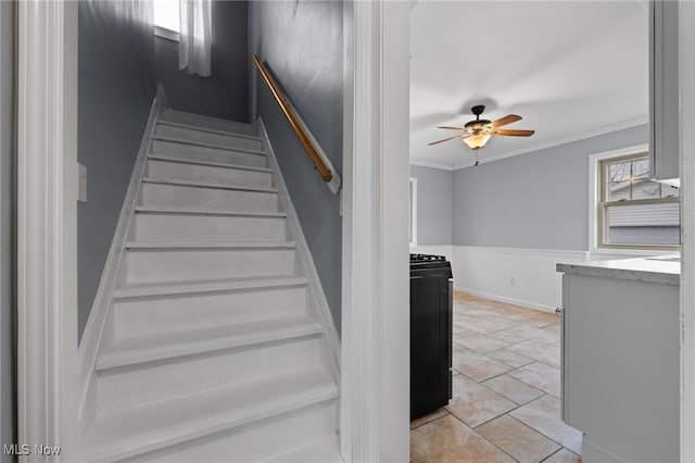 stairs featuring a wainscoted wall, ceiling fan, and ornamental molding