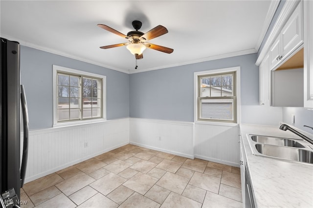 kitchen featuring a ceiling fan, wainscoting, freestanding refrigerator, light countertops, and a sink