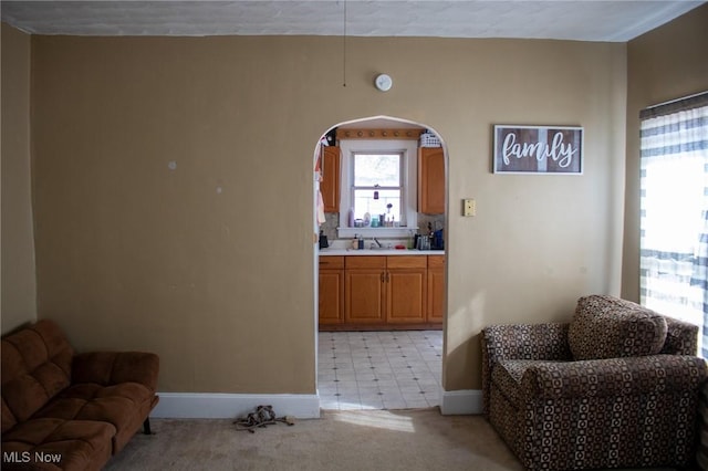 sitting room featuring arched walkways, light carpet, and baseboards