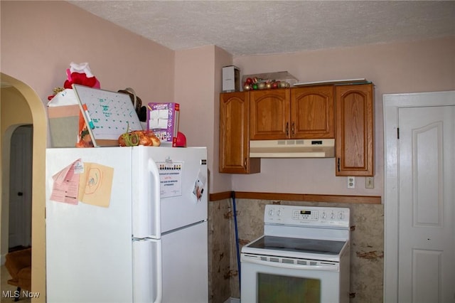 kitchen featuring white appliances, arched walkways, brown cabinetry, a textured ceiling, and under cabinet range hood