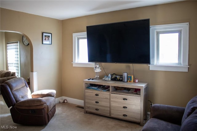 living area with a wealth of natural light, light colored carpet, arched walkways, and baseboards