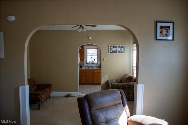 living area featuring arched walkways, ceiling fan, baseboards, and light colored carpet