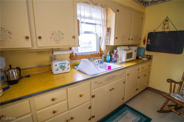 kitchen with white microwave, a sink, white cabinets, baseboards, and light countertops