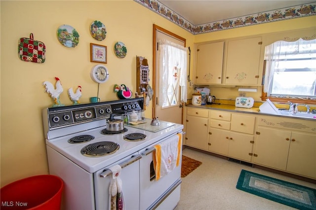 kitchen with white electric stove, cream cabinetry, and a healthy amount of sunlight