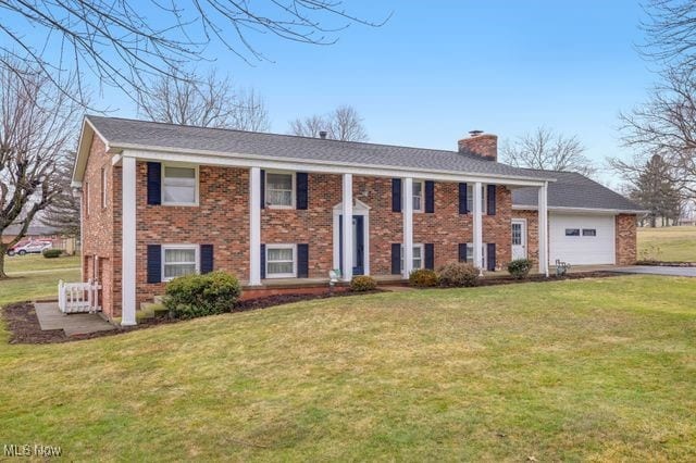 split foyer home featuring an attached garage, brick siding, driveway, a chimney, and a front yard