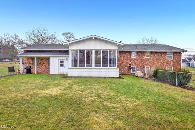 rear view of property with brick siding, a lawn, fence, and a sunroom