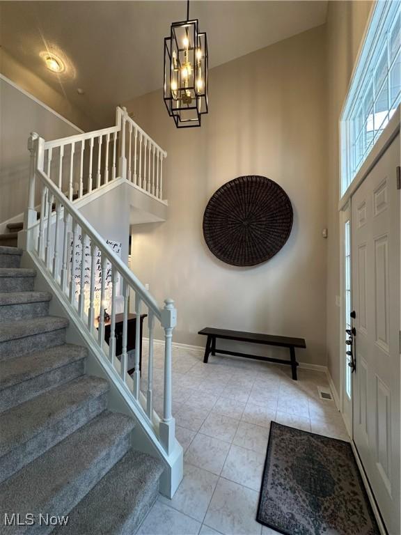 foyer entrance with tile patterned flooring, baseboards, a high ceiling, and an inviting chandelier