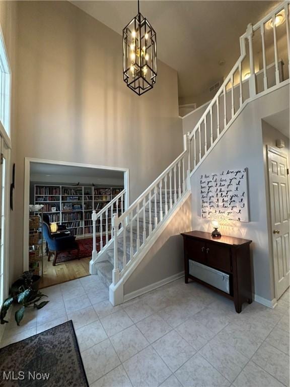 tiled entryway featuring a chandelier, a towering ceiling, baseboards, and stairs