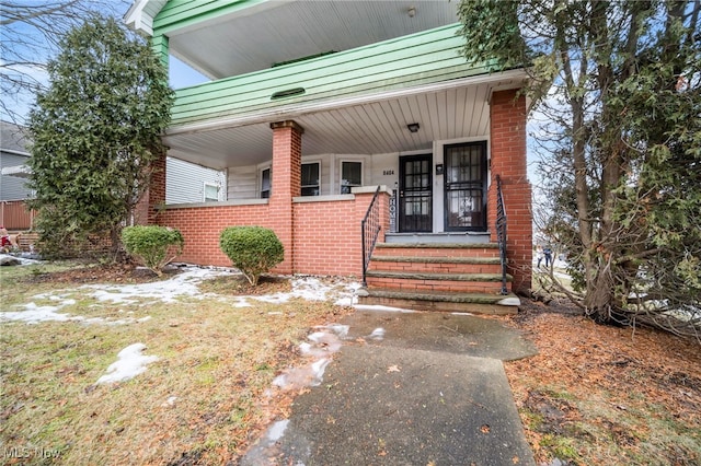 doorway to property featuring covered porch and brick siding