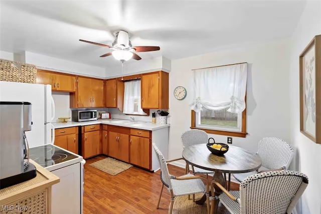 kitchen with white appliances, a sink, light wood-style floors, light countertops, and brown cabinetry