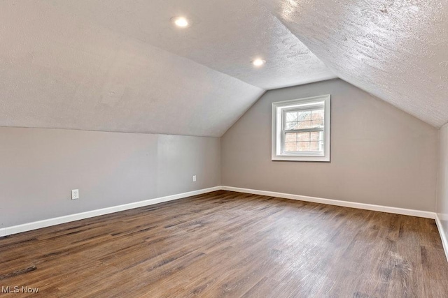 additional living space with vaulted ceiling, a textured ceiling, baseboards, and wood finished floors