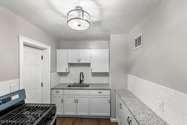 kitchen featuring stainless steel gas stove, visible vents, dark wood-style floors, white cabinetry, and a sink