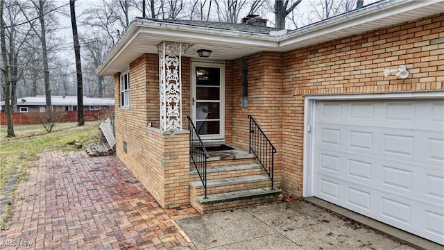 entrance to property featuring a garage, a chimney, decorative driveway, and brick siding