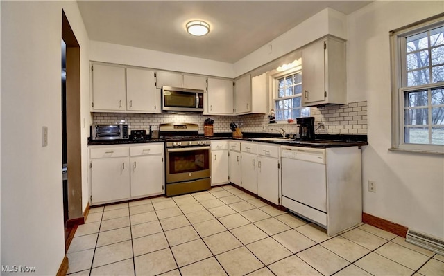 kitchen featuring stainless steel appliances, dark countertops, a sink, and backsplash