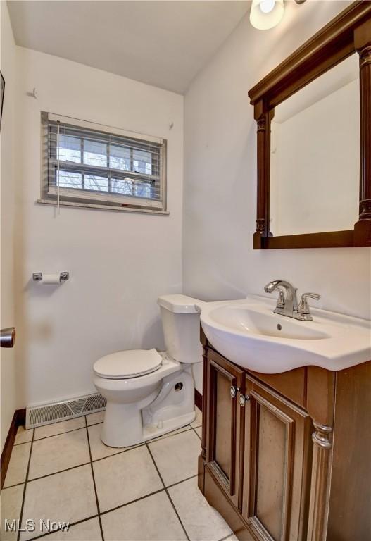 half bathroom featuring visible vents, toilet, vanity, tile patterned flooring, and baseboards