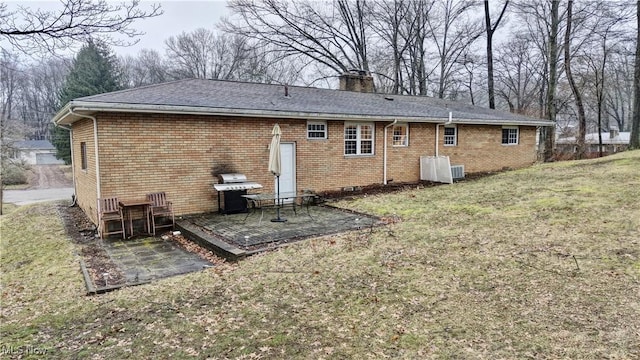 back of property featuring a yard, brick siding, a chimney, and a patio