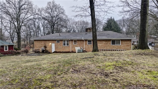 back of property featuring central air condition unit, a chimney, a lawn, and brick siding