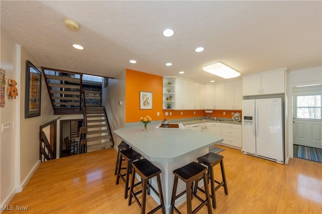 kitchen with light wood-style flooring, white refrigerator with ice dispenser, a peninsula, and a breakfast bar area