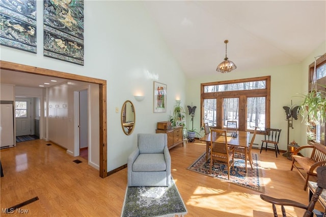 foyer entrance with high vaulted ceiling, light wood-style flooring, baseboards, and an inviting chandelier