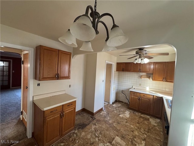 kitchen featuring arched walkways, decorative backsplash, a ceiling fan, brown cabinets, and light countertops