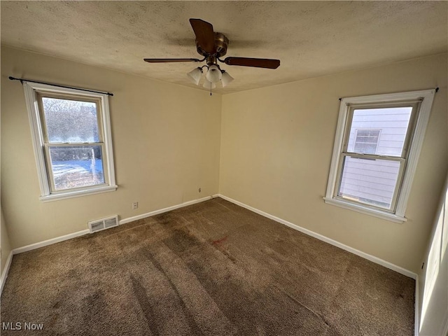 unfurnished room featuring baseboards, visible vents, dark carpet, and a textured ceiling