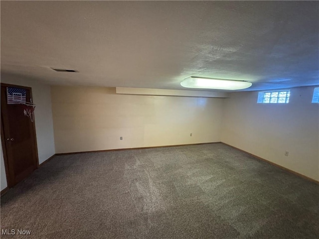 basement featuring a textured ceiling, carpet floors, visible vents, and baseboards