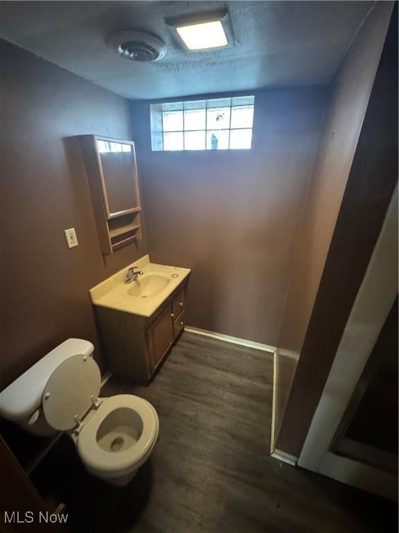 half bathroom with vanity, wood finished floors, and toilet