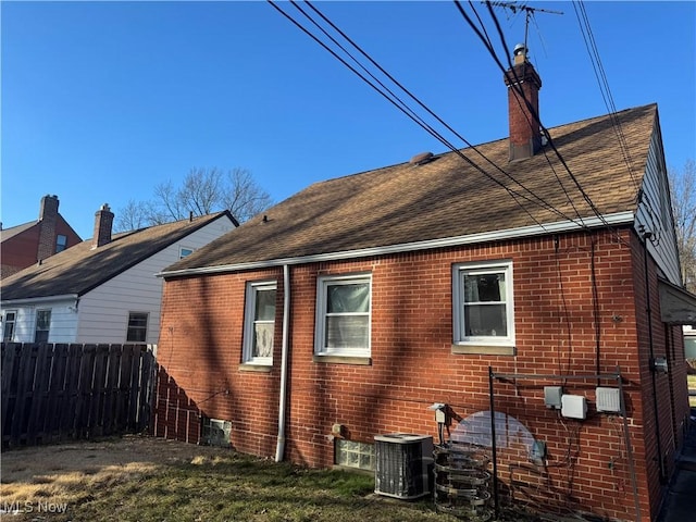 view of property exterior with roof with shingles, a chimney, fence, and brick siding