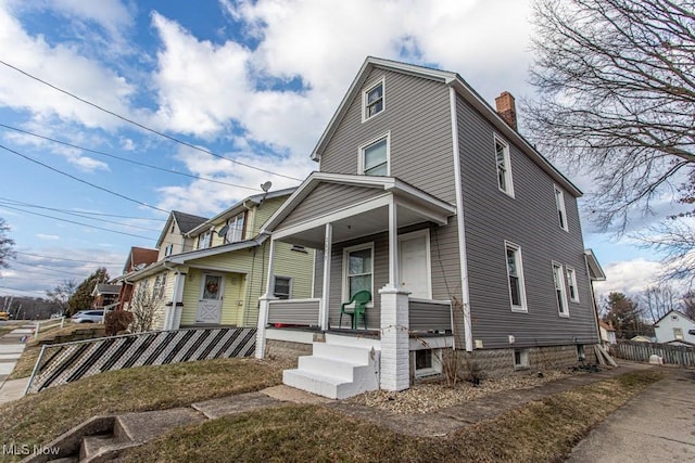 view of front of home featuring a porch, fence, and a chimney