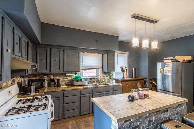 kitchen featuring light wood-style floors, freestanding refrigerator, white range with gas cooktop, a sink, and under cabinet range hood