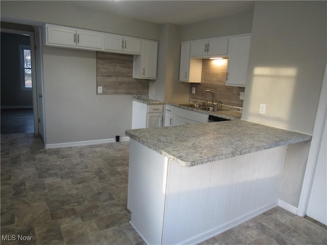 kitchen with baseboards, decorative backsplash, a peninsula, white cabinetry, and a sink