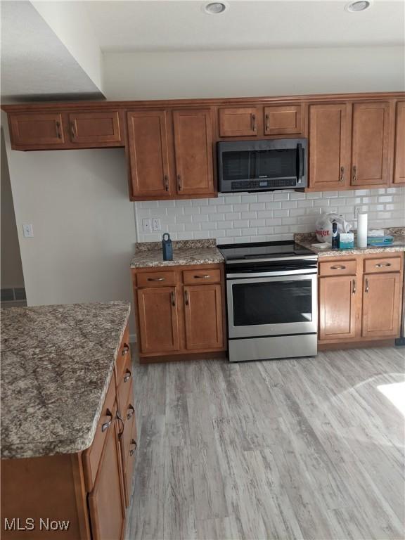 kitchen featuring stainless steel appliances, light wood-style floors, decorative backsplash, and brown cabinets