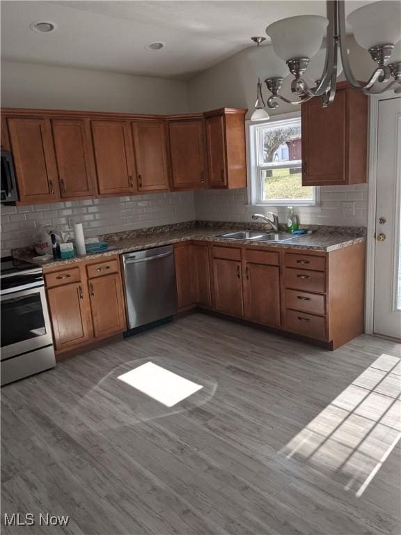 kitchen with appliances with stainless steel finishes, a sink, light wood-style floors, and brown cabinets