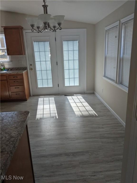 doorway to outside with a notable chandelier, light wood finished floors, and a healthy amount of sunlight