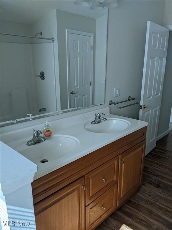 full bathroom featuring double vanity, walk in shower, a sink, and wood finished floors