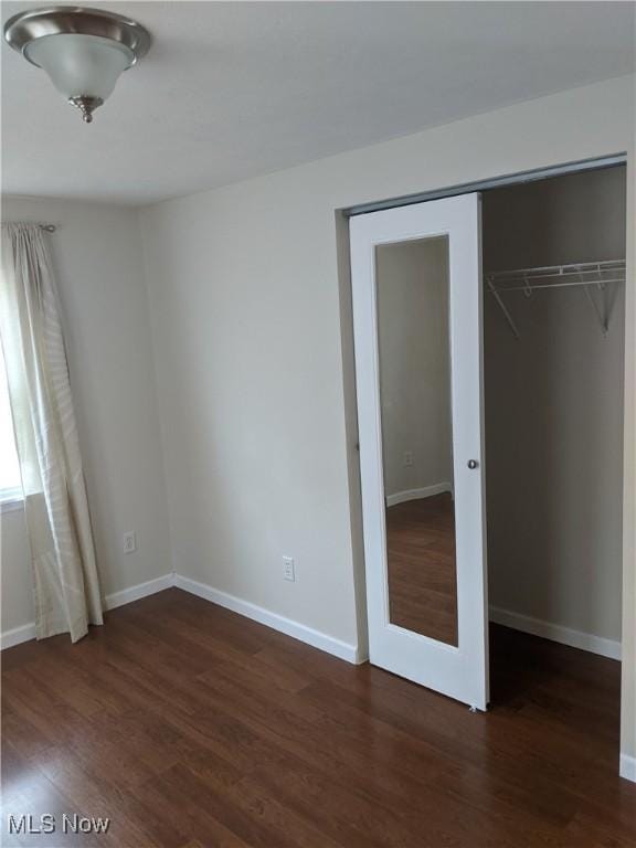 unfurnished bedroom with a closet, baseboards, and dark wood-style flooring