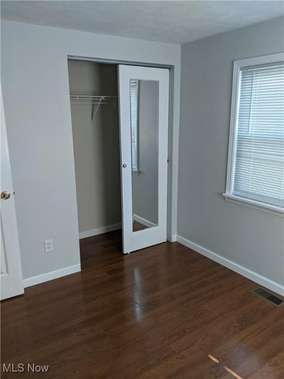 unfurnished bedroom with baseboards, a closet, visible vents, and wood finished floors