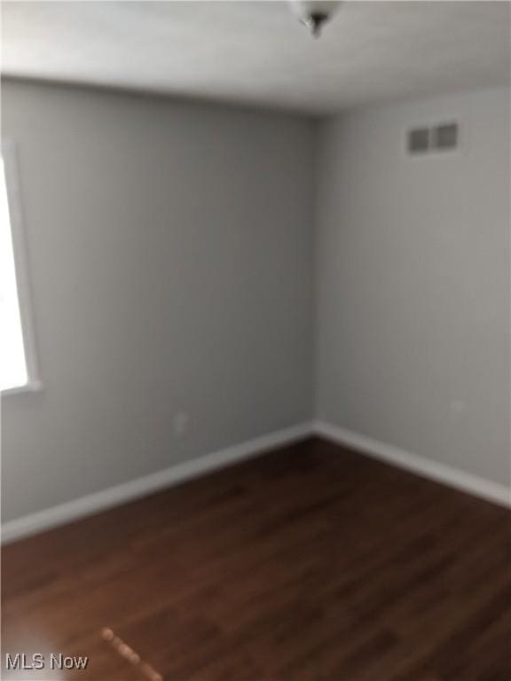 empty room featuring dark wood-type flooring, visible vents, and baseboards