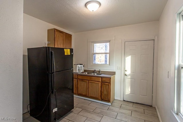 kitchen featuring baseboards, brown cabinetry, freestanding refrigerator, a textured ceiling, and a sink