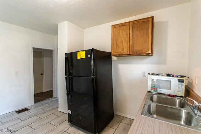 kitchen with visible vents, white microwave, brown cabinetry, freestanding refrigerator, and a sink