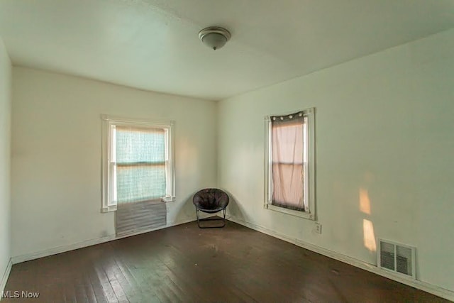 empty room featuring a wealth of natural light, visible vents, and hardwood / wood-style floors