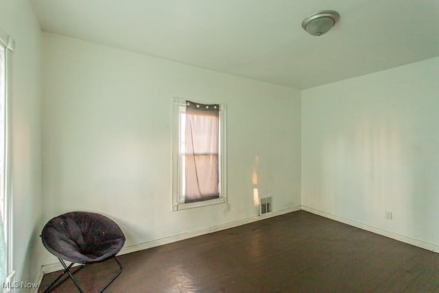 empty room with dark wood-style flooring, visible vents, and baseboards