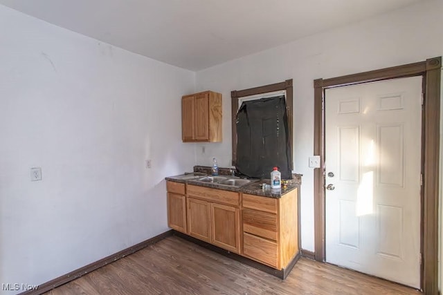 kitchen with wood finished floors, dark countertops, a sink, and baseboards