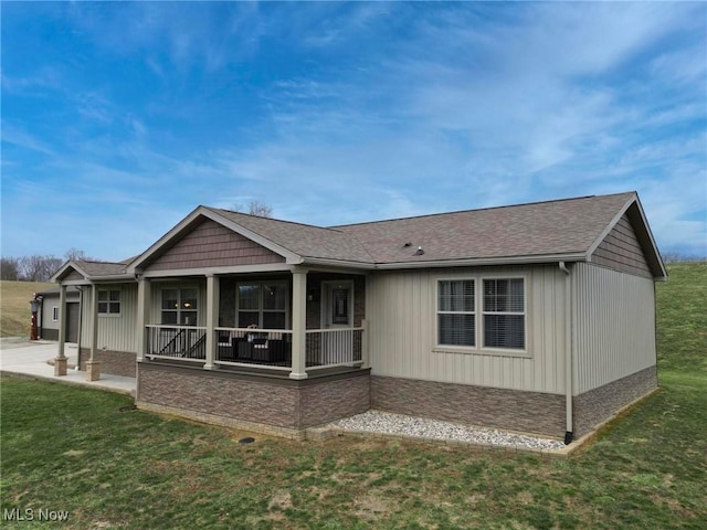 back of property featuring a porch, concrete driveway, roof with shingles, and a yard